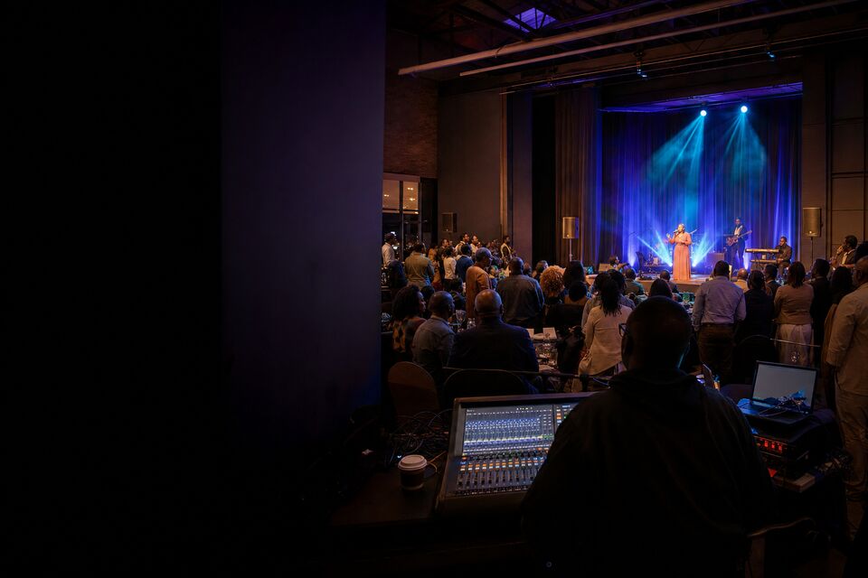 A live show seen from the control position, an engineer at a console before a lit stage