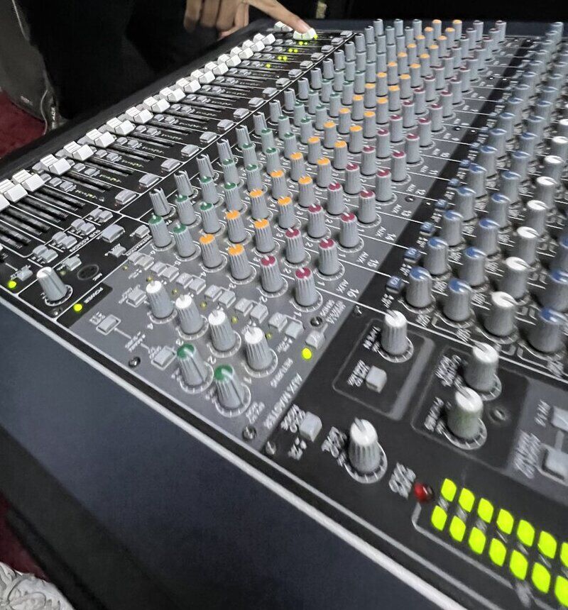 A hand adjusting a channel on a large mixing console, level meters glowing
