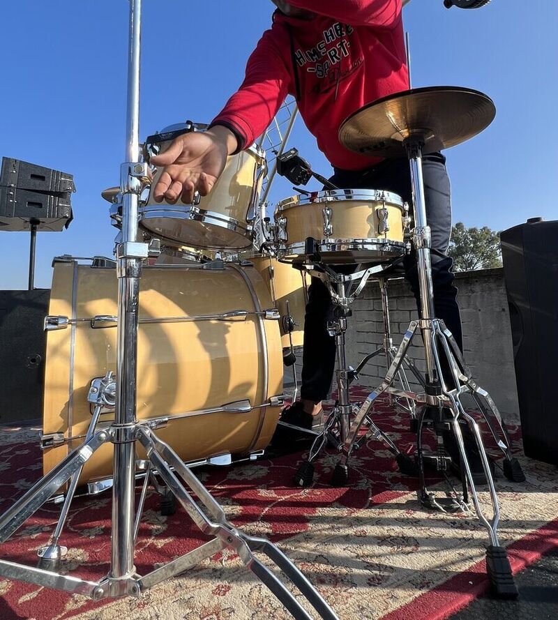 A drummer's hands adjusting a gold drum kit on an outdoor stage