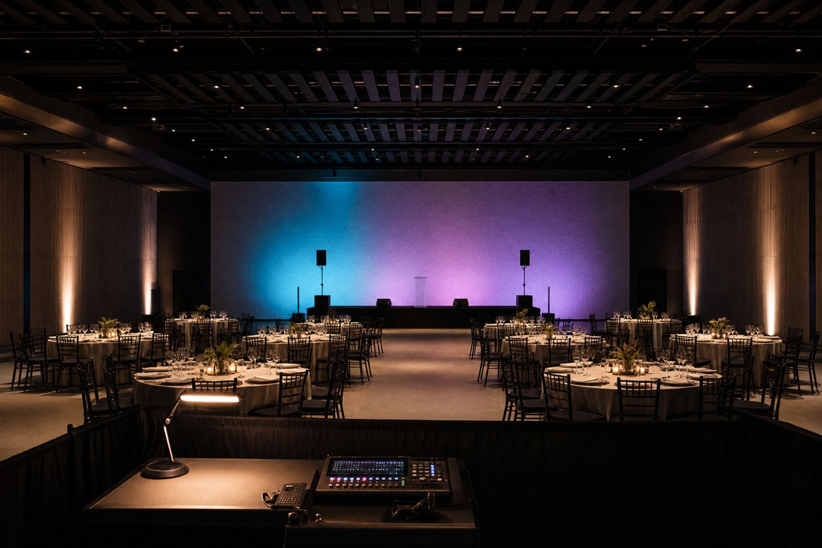 A finished, empty event venue moments before doors open — stage washed in cyan and violet, chairs aligned, control position tidy